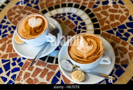 Zwei mit 'Kaffee Kunst' schaumigen tops Cappuccino auf einem Mosaik Tisch mit Marmorplatte Stockfoto