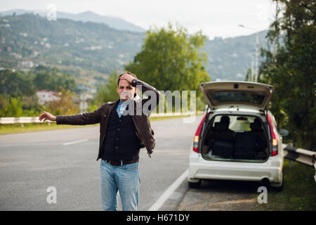 Trampen - Laufwerke. Junger Mann mit erhobener Hand vor Auto unterwegs Stockfoto