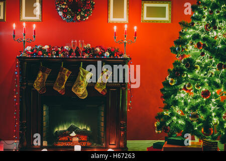 Schön geschmückten Weihnachtsbaum mit roten und bzw. bernsteingelben Flitter und Girlande, im neuen Jahr Hintergrund mit Kamin und Socken Stockfoto