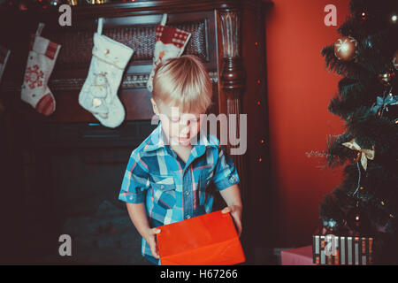 Schöne Portrait eines kleinen Jungen mit einem Geschenk in der Hand im neuen Jahr Zimmer mit einem Weihnachtsbaum. Die Idee für Postkarten. soft Schwerpunkte Stockfoto