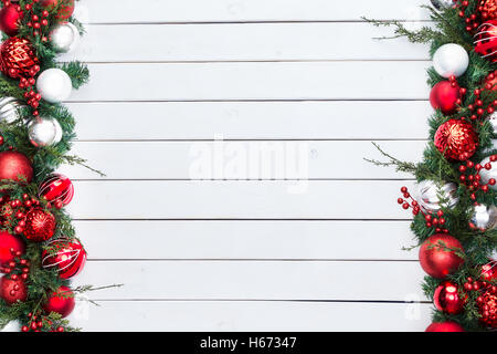 Doppelseitige festliche rote und silberne Kugeln in einer Weihnachts-Grenze mit frischen Blätter und Beeren über rustikale weiß gebeizt Holz Stockfoto