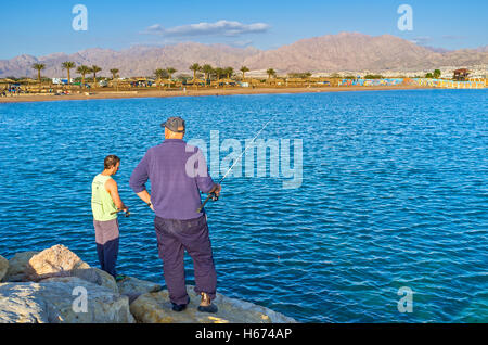 Die Männer Angeln von der Mole mit der Berglandschaft von Aqaba im Hintergrund, Eilat Stockfoto