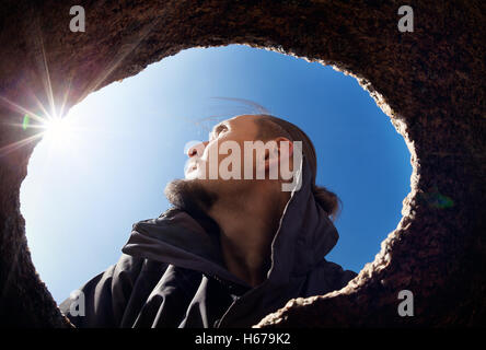 Porträt des Mannes aus dem Loch der Höhle in der Wüste am blauen Himmel mit Sonne flare Stockfoto