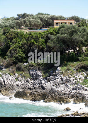 Wellen gegen Felsen am östlichen Ende von St. Spiridon Beach, Korfu Griechenland, unten schöne Villa mit Infinity-pool Stockfoto