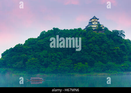 Sonnenuntergang Himmel über Tourist cruise Boot am Fluss Kiso mit Inuyama Burg Festung auf einem Waldhügel an einem Sommerabend Stockfoto