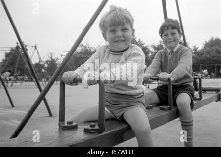 Jungen auf einer Bank in einem öffentlichen Park in 1960er Jahren Großbritannien schwingen Stockfoto