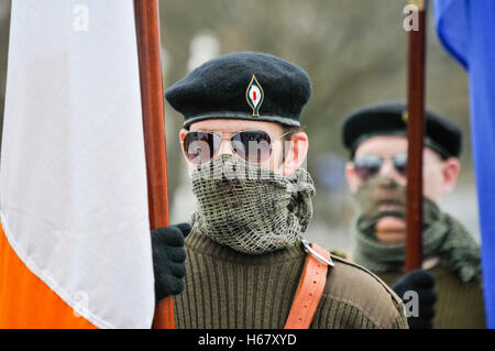 Männer, gekleidet in Irischen paramilitärischen Uniformen, deren Gesichter vom Militärischen scrim Schals erfassten Irische Flaggen in Milltown Friedhof, während der Hauptversammlung Stockfoto