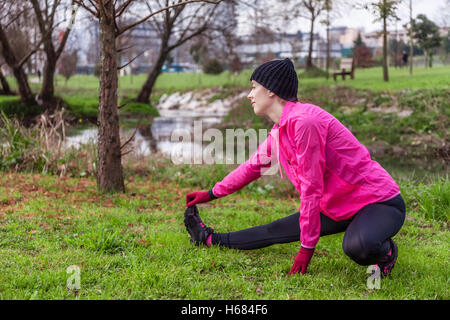 Junge Frau Aufwärmen und Dehnen der Beine vor der Ausführung an einem kalten Wintertag in einem städtischen Park. Stockfoto