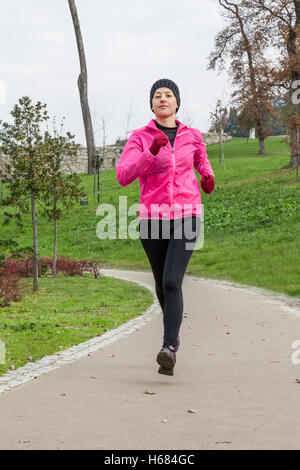 Junge Frau läuft an einem kalten Wintertag in einem städtischen Park. Stockfoto