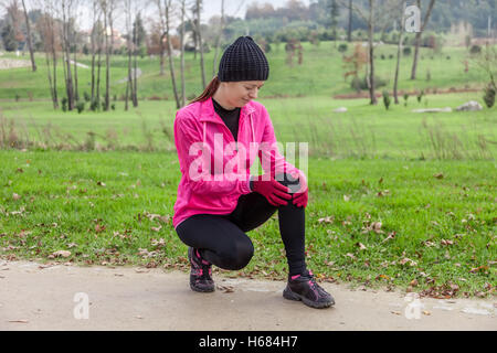 Junge Sportlerin verletzt von einer Knieverletzung an einem kalten Wintertag auf dem Weg von einem städtischen Park. Stockfoto