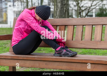 Junge Sportler Frau müde oder depressiv, ruht auf einer Bank an einem kalten Wintertag in den Spuren von einem städtischen Park. Stockfoto