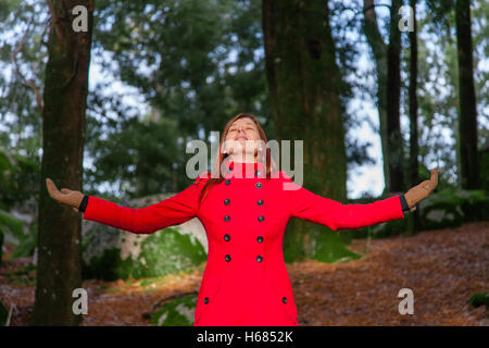 Frau, genießen die Wärme des Sonnenlichts auf einen Wald tragen einen roten Mantel winter Stockfoto