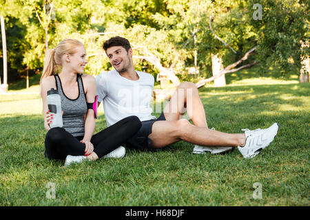 Gesunder Mann und Frau ruht nach dem Training und Trinkwasser beim Sitzen auf dem Rasen Stockfoto