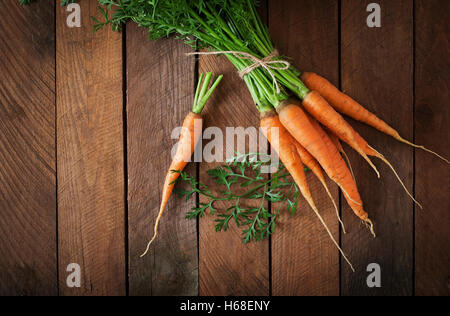 Handvoll frische Karotten mit grünen Blättern über hölzerne Hintergrund. Ansicht von oben Stockfoto