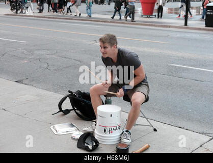 Junger Erwachsener gesehen, improvisierte Schlagzeug in einer belebten Innenstadt entfernt während der Rush Hour. Das Bild zeigt ihn auf Eimer zu spielen. Stockfoto