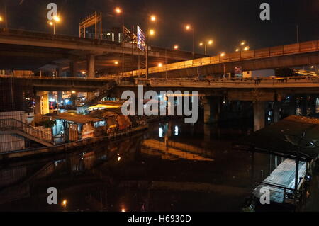 Ein Slum unter mehreren Autobahnen in die Mutter auf, District, Bangkok, Thailand entlang des Flusses in der Nacht. Stockfoto