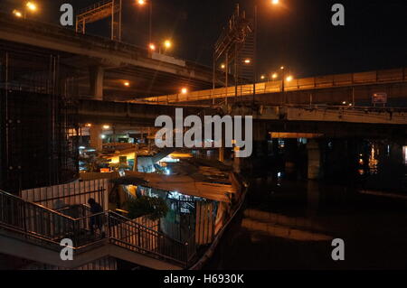 Ein Slum unter mehreren Autobahnen in die Mutter auf, District, Bangkok, Thailand entlang des Flusses in der Nacht. Stockfoto