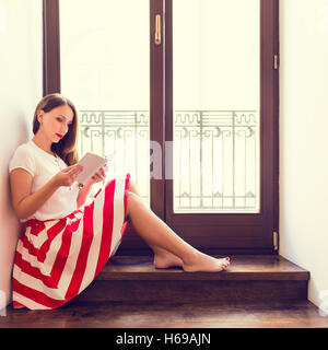 Junge stilvolle Dame Buch in der Nähe von Balkon Glastür. Schöne Mädchen mit Buch über Holztreppen im hotel Stockfoto