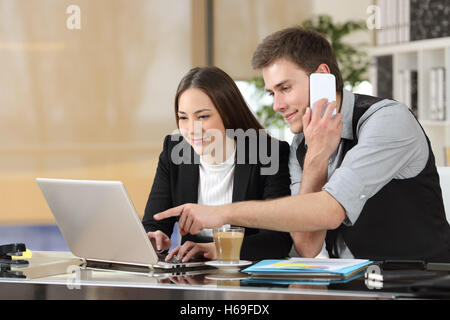 Zwei Kollegen zusammen online gebende Anweisungen mit einem Laptop arbeiten und ruft auf dem Handy in einem Schreibtisch im Büro Stockfoto