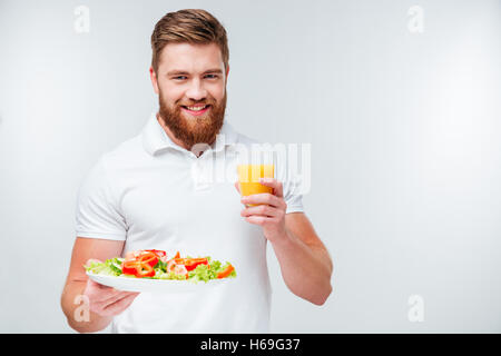 Glücklich fröhlich bärtiger Mann Halteplatte mit Gemüse und Glas orange Juiceisolated auf weißem Hintergrund Stockfoto