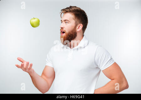 Glücklich lässig junger Mann warf einen grünen Apfel, isoliert auf weißem Hintergrund Stockfoto