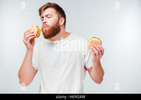 Junge bärtige Mann mit Augen geschlossen genießen Essen Hamburger isoliert auf weißem Hintergrund Stockfoto