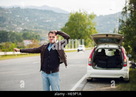 Trampen - Laufwerke. Junger Mann mit erhobener Hand vor Auto unterwegs Stockfoto