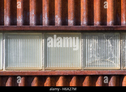 Enge, von Rusty Wellpappe Metall Wand mit drei Glasbausteine, eines davon ist Broken Stockfoto