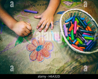 Kind mit einem Korb voller Wachs Zeichnung Buntstifte über Handwerk Geschenkpapier. Erhöhte Ansicht Stockfoto