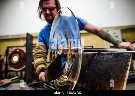 Spezialist für Glasbläser James Devereux verwendet eine hölzerne Paddel, um eine Scheibe aus geschmolzenem Glas zu gestalten, wie er klar Glas Rondelle für eine Skulptur in seiner Werkstatt in Wiltshire. Stockfoto