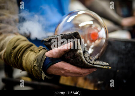 Spezialist für Glasbläser James Devereux verwendet nasse Zeitung, um eine Stück aus geschmolzenem Glas zu gestalten, wie er klar Glas Rondelle für eine Skulptur in seiner Werkstatt in Wiltshire. Stockfoto