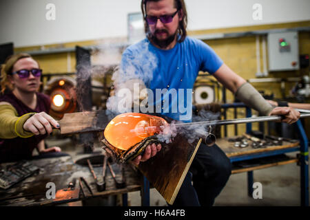 Spezialist für Glasbläser James Devereux verwendet nasse Zeitung, um eine Stück aus geschmolzenem Glas zu gestalten, wie er klar Glas Rondelle für eine Skulptur in seiner Werkstatt in Wiltshire. Stockfoto