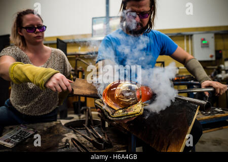 Spezialist für Glasbläser James Devereux verwendet nasse Zeitung, um eine Stück aus geschmolzenem Glas, assistiert von Katherine Huskie, da er klar Glas Rondelle für eine Skulptur in seiner Werkstatt in Wiltshire zu gestalten. Stockfoto