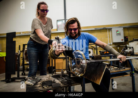 Spezialist für Glasbläser James Devereux verwendet Metall Bremssättel, um eine Stück aus geschmolzenem Glas, assistiert von Katherine Huskie, da er klar Glas Rondelle für eine Skulptur in seiner Werkstatt in Wiltshire zu gestalten. Stockfoto