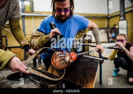 Spezialist für Glasbläser James Devereux verwendet Metall Bremssättel, um eine Stück aus geschmolzenem Glas zu gestalten, wie er klar Glas Rondelle für eine Skulptur in seiner Werkstatt in Wiltshire. Stockfoto