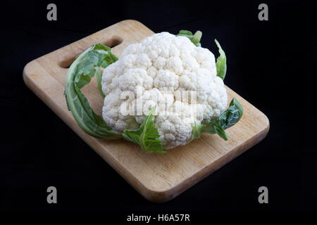 Blumenkohl in grünes Blatt auf hölzernen Steckbrett auf schwarzem Hintergrund Stockfoto