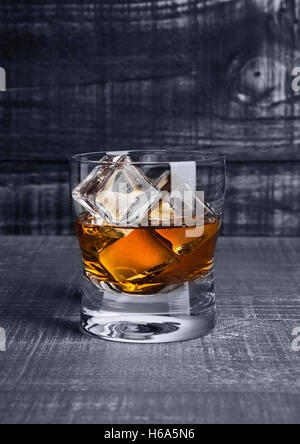 Glas Whiskey mit Eiswürfeln auf blauem Hintergrund aus Holz Stockfoto