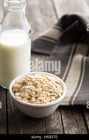 Trockene gewalzte Haferflocken in die Schüssel und Milch im Glas. Stockfoto