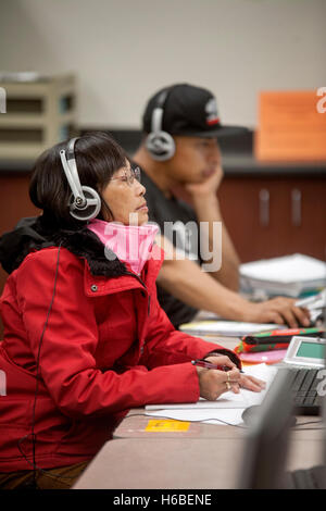 Einen mittleren Alters asiatischen weiblichen Santa Ana, CA, Community College-Student arbeitet bei einem Learning Skills center Computer-Monitor. Hinweis: Kopfhörer und Hispanic Kursteilnehmer im Hintergrund. Stockfoto