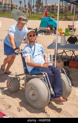 Ein behinderter Mann wird auf einen speziellen Rollstuhl mit extra großen Ballonreifen geschoben, Sand in Huntington Beach, Kalifornien zu verhandeln. Stockfoto