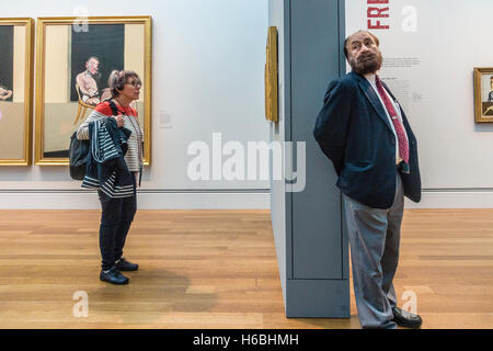 Eine ältere Frau mit ihrem Kopfhörer audio Tour und ein Museumswächter teilen einen Raum im Museum durch eine Mauer getrennt. Stockfoto