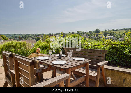 Ein Gartentisch & Stühle set mit legen Sie Einstellungen & Wein für eine Mahlzeit mit Blick über den Cotswold Hills bei Nailsworth, UK Stockfoto