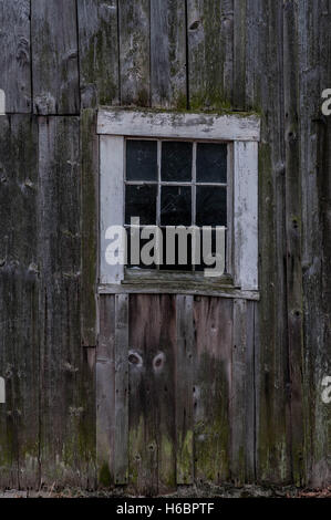 Ein zerbrochenes Fenster auf eine alte hölzerne Scheune. Stockfoto