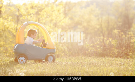 Ein drei-jähriger Junge spielt in einem Spielzeugauto im goldenen Licht des späten Nachmittags. Stockfoto