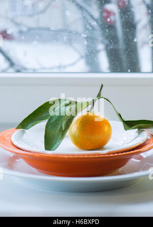 Mandarine mit einem Zweig und Blätter auf Platte vor dem Hintergrund des Fensters den Schnee Stockfoto