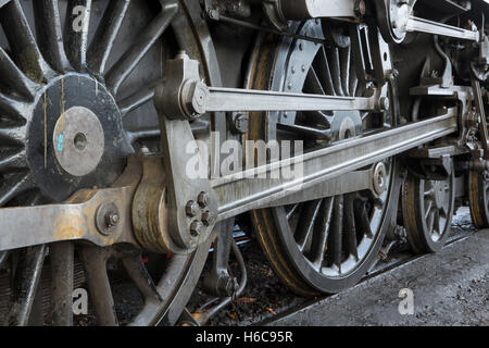 Detailansicht des Laufganges von einem Dampfzug. Großes Rad im Vordergrund mit Kolbenstange in der Vollbildansicht auf Vorderräder. Stockfoto