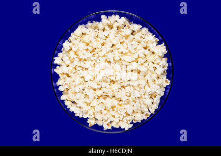 Fertiges Popcorn in eine blaue Glasschale auf blauem Hintergrund. Schmetterling-förmige Popcorn aufgeblasen aus den Kernen. Stockfoto