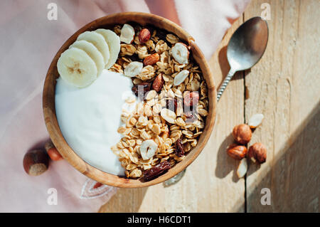 Hausgemachte Haferflocken Müsli mit Nüssen, Rosinen und Banane in Holzschale, sonnigen Morgen Stockfoto