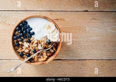 Hausgemachte Haferflocken Müsli mit Erdnüssen, Heidelbeere und Banane in Holzschale, sonnigen Morgen Stockfoto