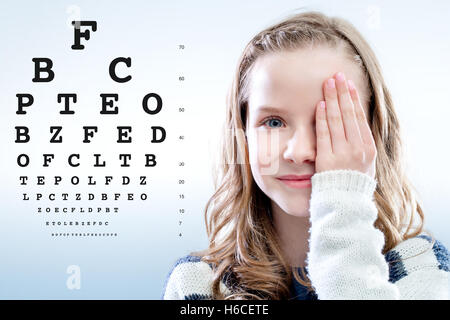 Porträt eines Mädchens, die Überprüfung der Sehkraft schließen Auge mit der Hand hautnah. Test-Chart im Hintergrund. Stockfoto